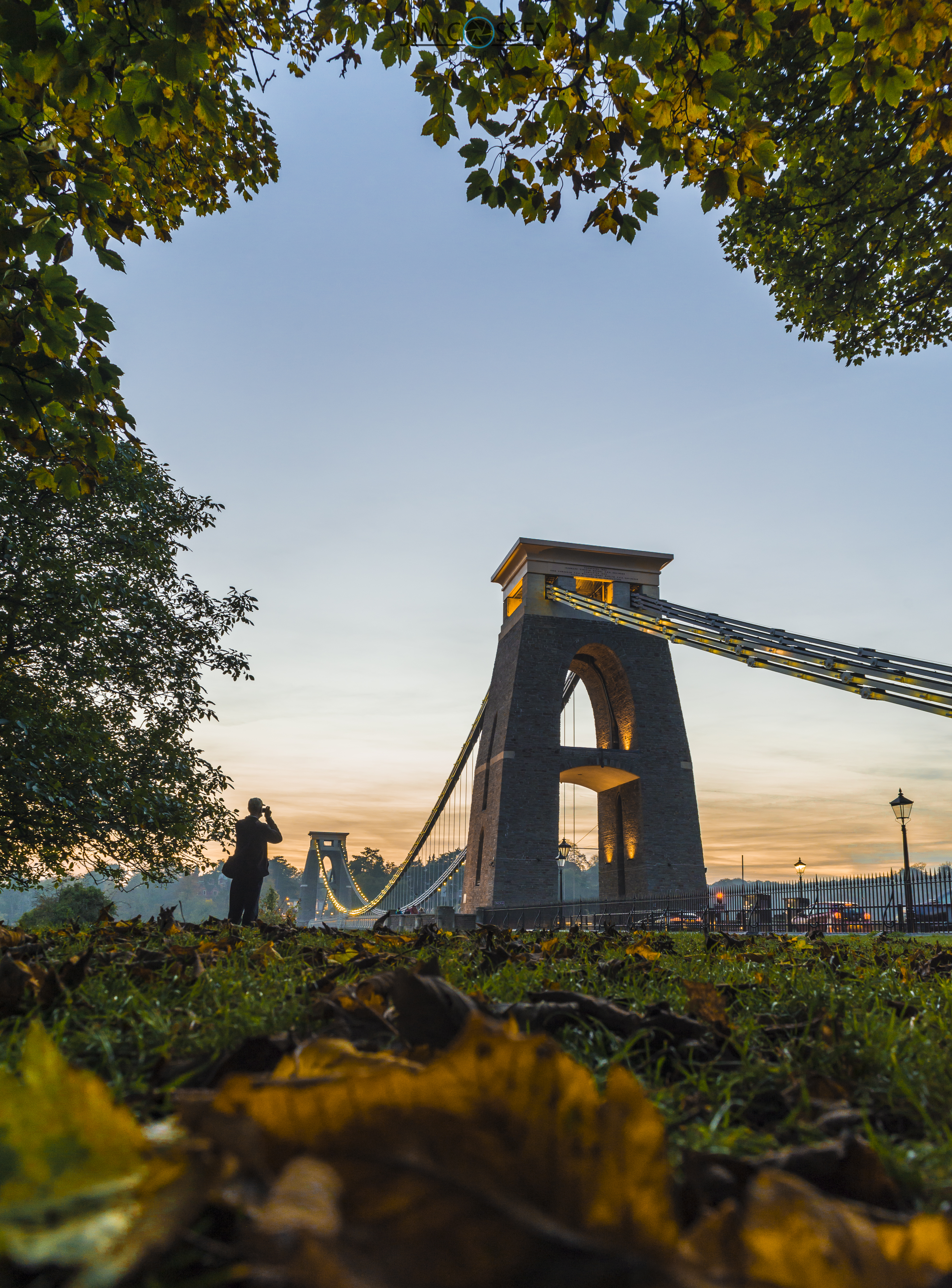 Clifton Suspension Bridge at dusk, framed by leaves.