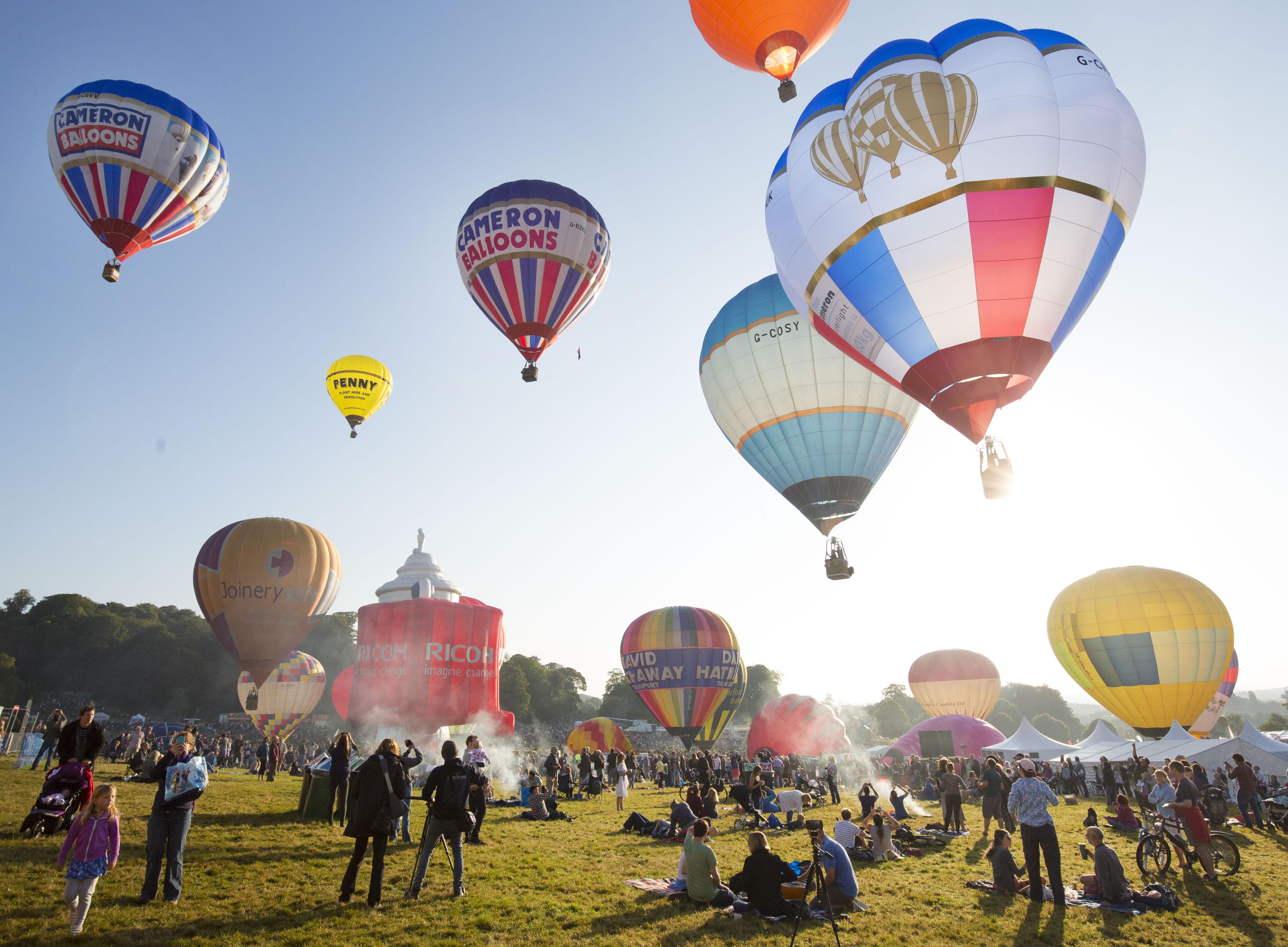Hot air balloons filling the sky at Bristol Balloon Festival, as onlookers look up.