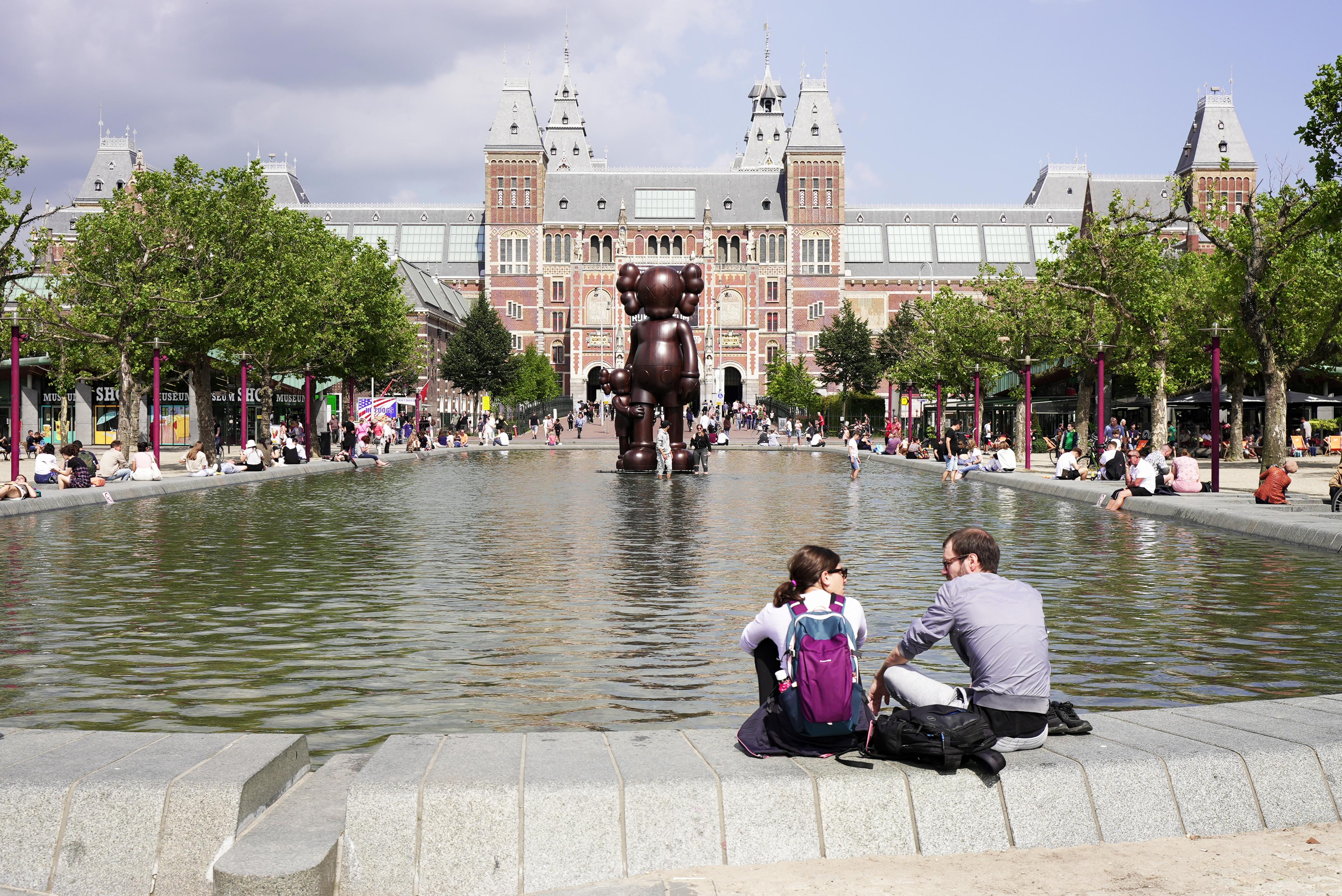 People sitting on the edge of water outside the Rijksmuseum in Amsterdam.